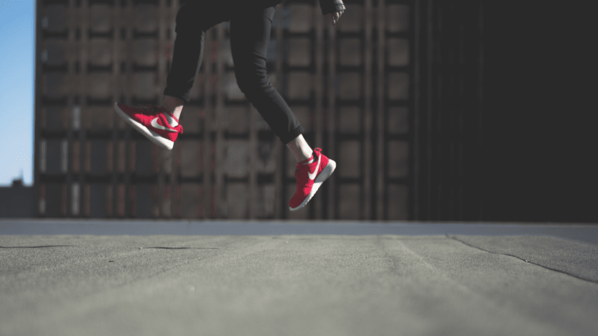 Ihmisen jalat hypähtämässä ilmaan punaiset tennarit jalassa.